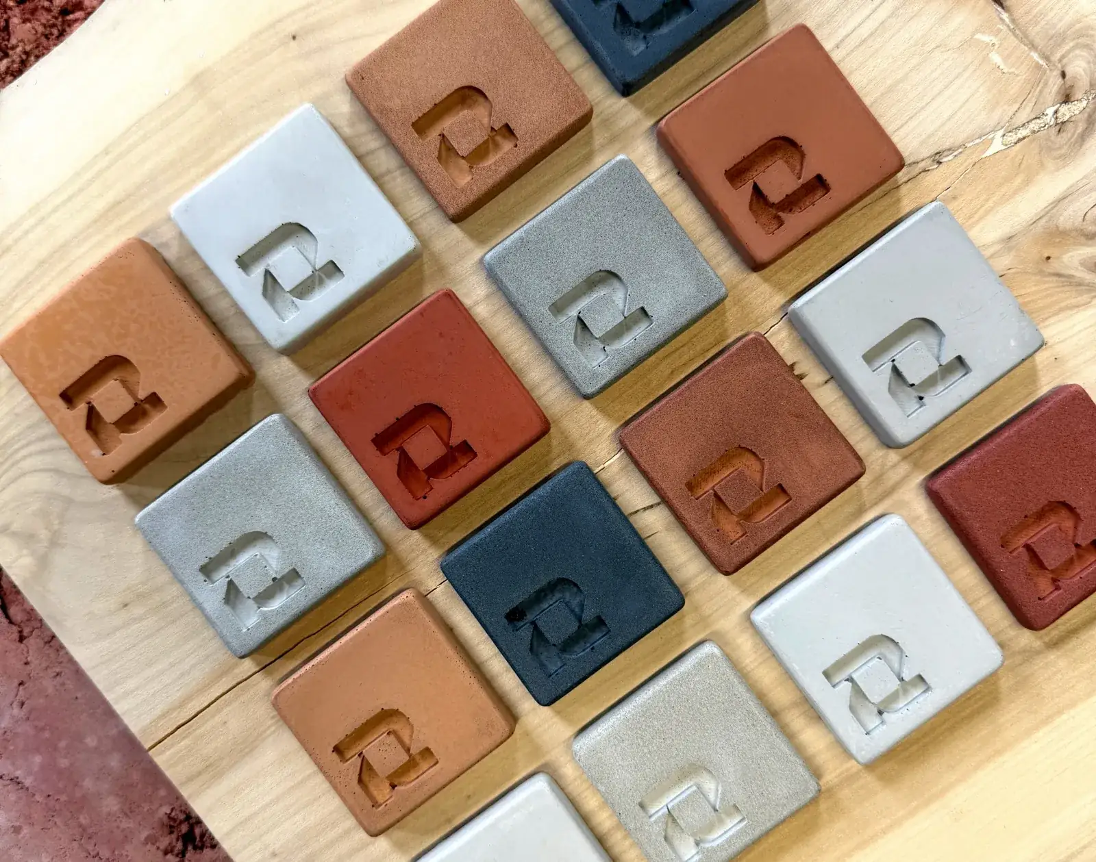 ROKA concrete sample tablets in every colour, from white and grey to charcoal, terracotta and red, laid on an oak slab