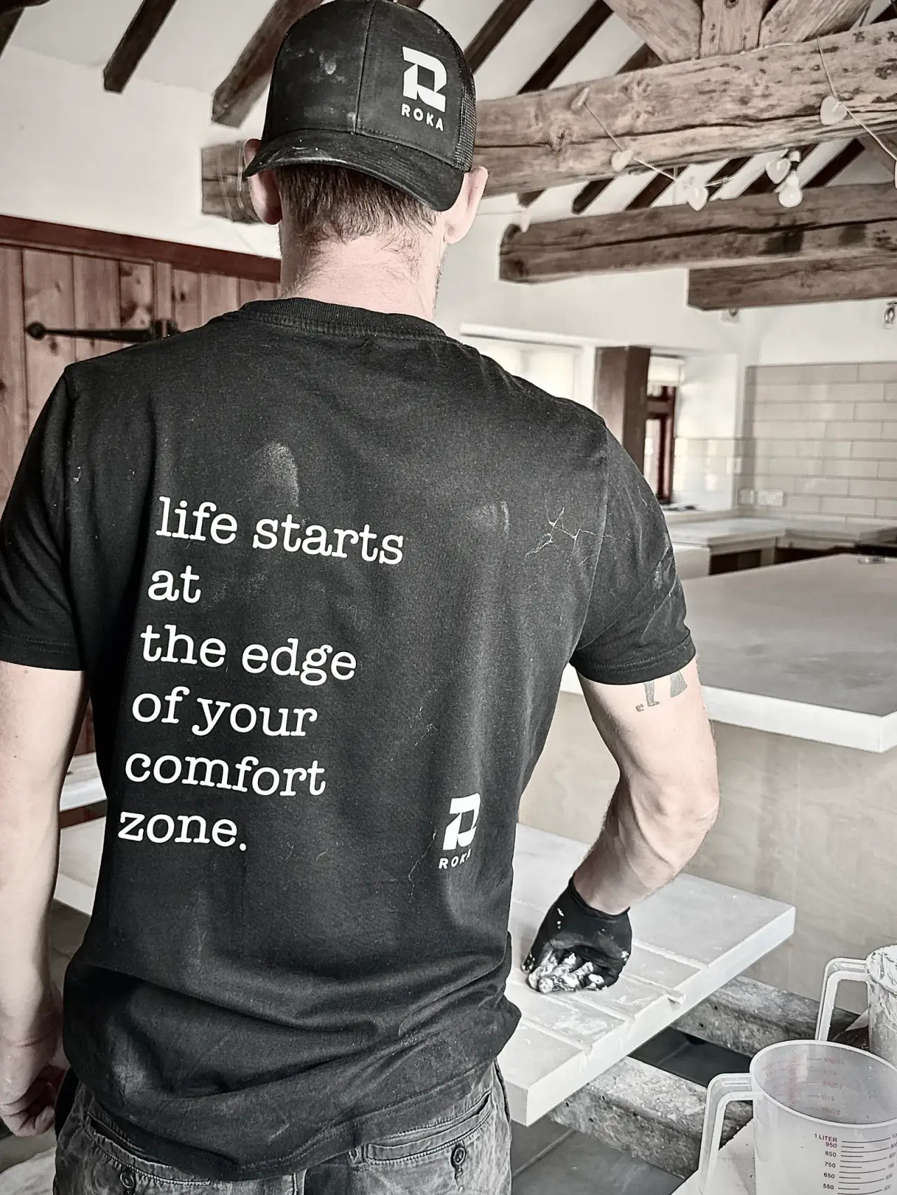 Aaron from behind in a ROKA T-shirt, finishing a concrete worktop with drainer grooves in a beamed barn kitchen