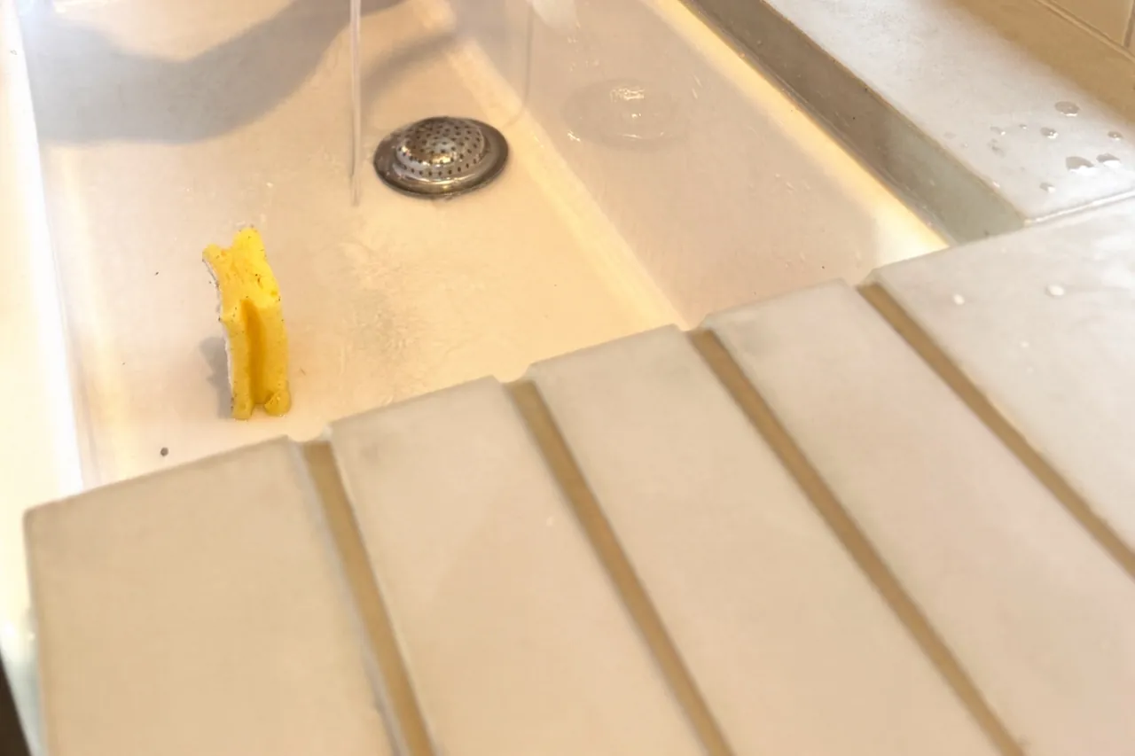 White Butler sink with water running to the drain, the concrete worktop overhanging its rim and drainer grooves cast into the surface