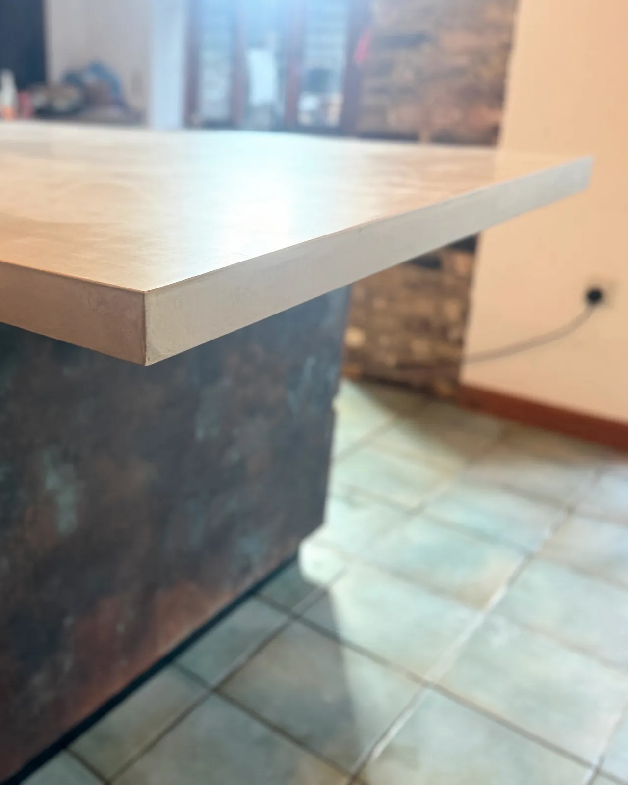 Corner of the concrete top overhanging the copper-finish end of the island, showing its 60 mm edge