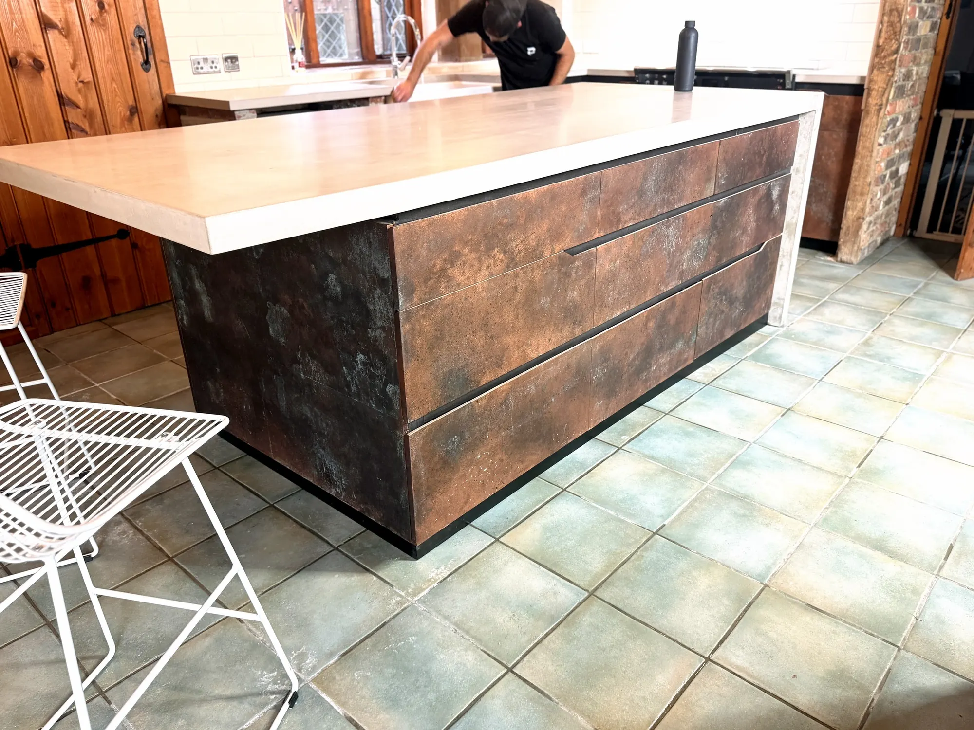 The whole concrete island from the breakfast-bar end: the top overhanging a copper-finish end panel, drawers along the side and the waterfall end beyond
