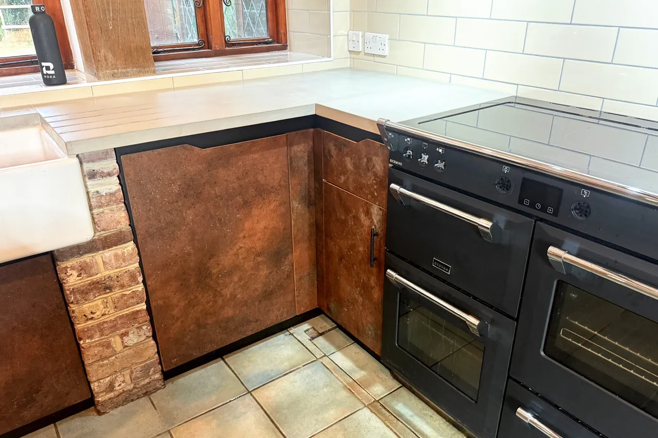 Concrete worktop running from the Butler sink, over a brick pillar and copper-finish doors, to a black range cooker in the corner